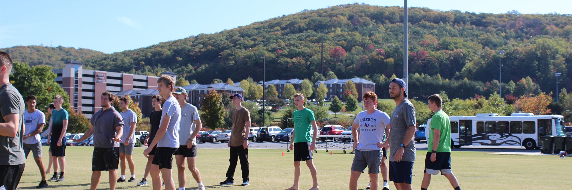 A line of young men standing together on a field, wooded hills behind them