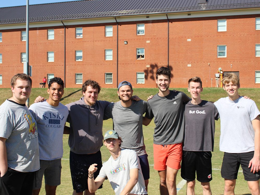 Eight young men standing arm in arm on a field after a workout, smiling at the camera
